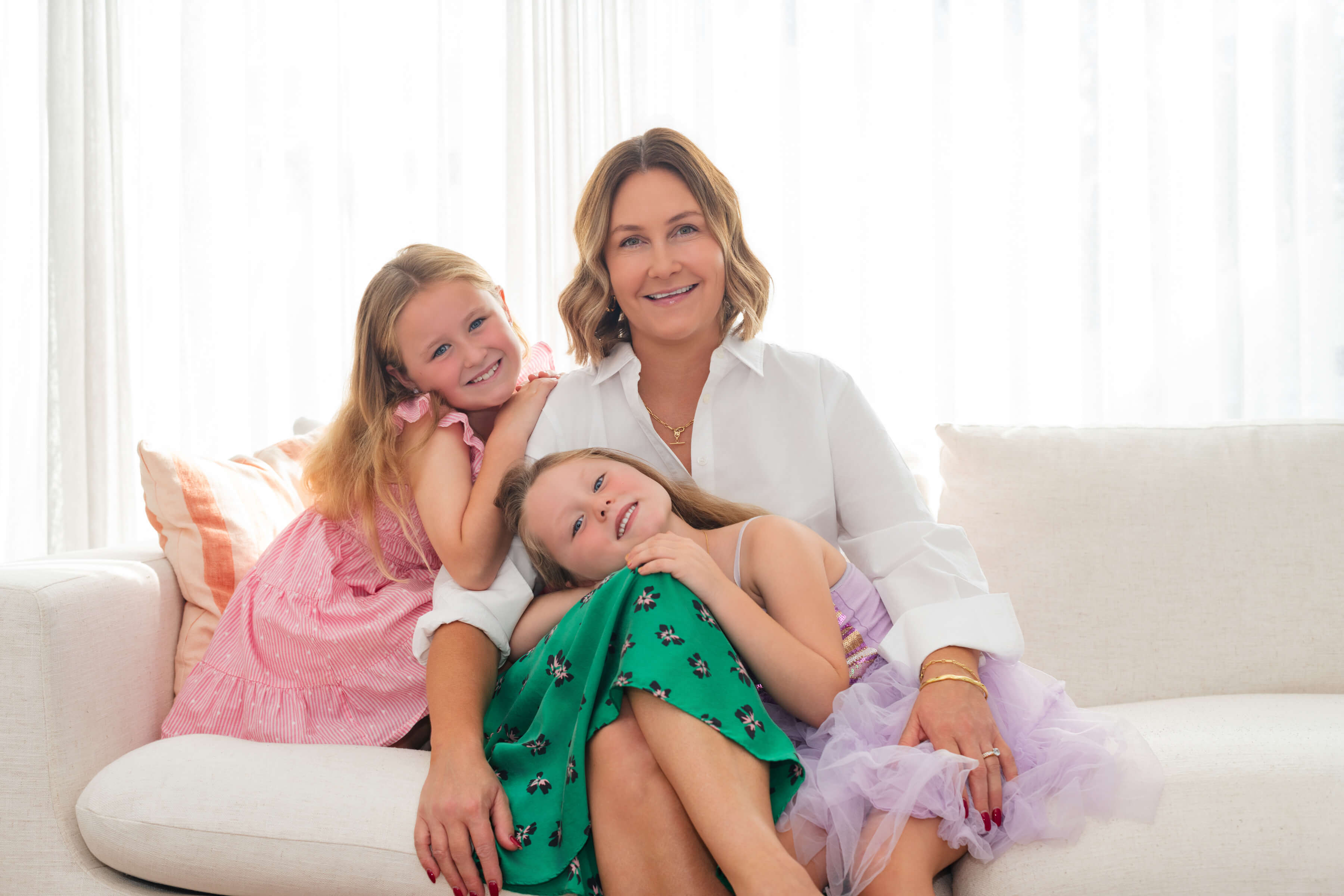 Image of Sonja Wilson, Founder of Bloom Squad Kids Haircare with her two daughters sitting on a couch in a bright room.